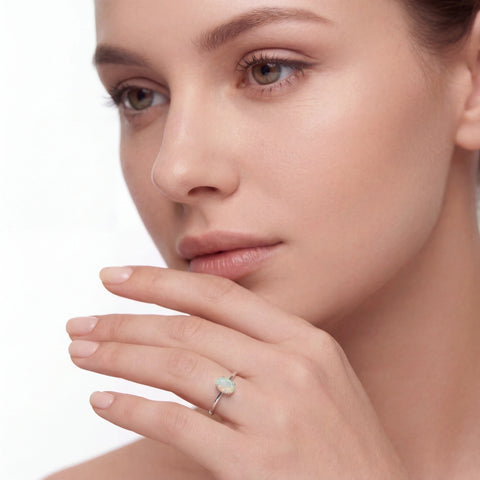 Close-up of a woman's face wearing an opal ring on a white background