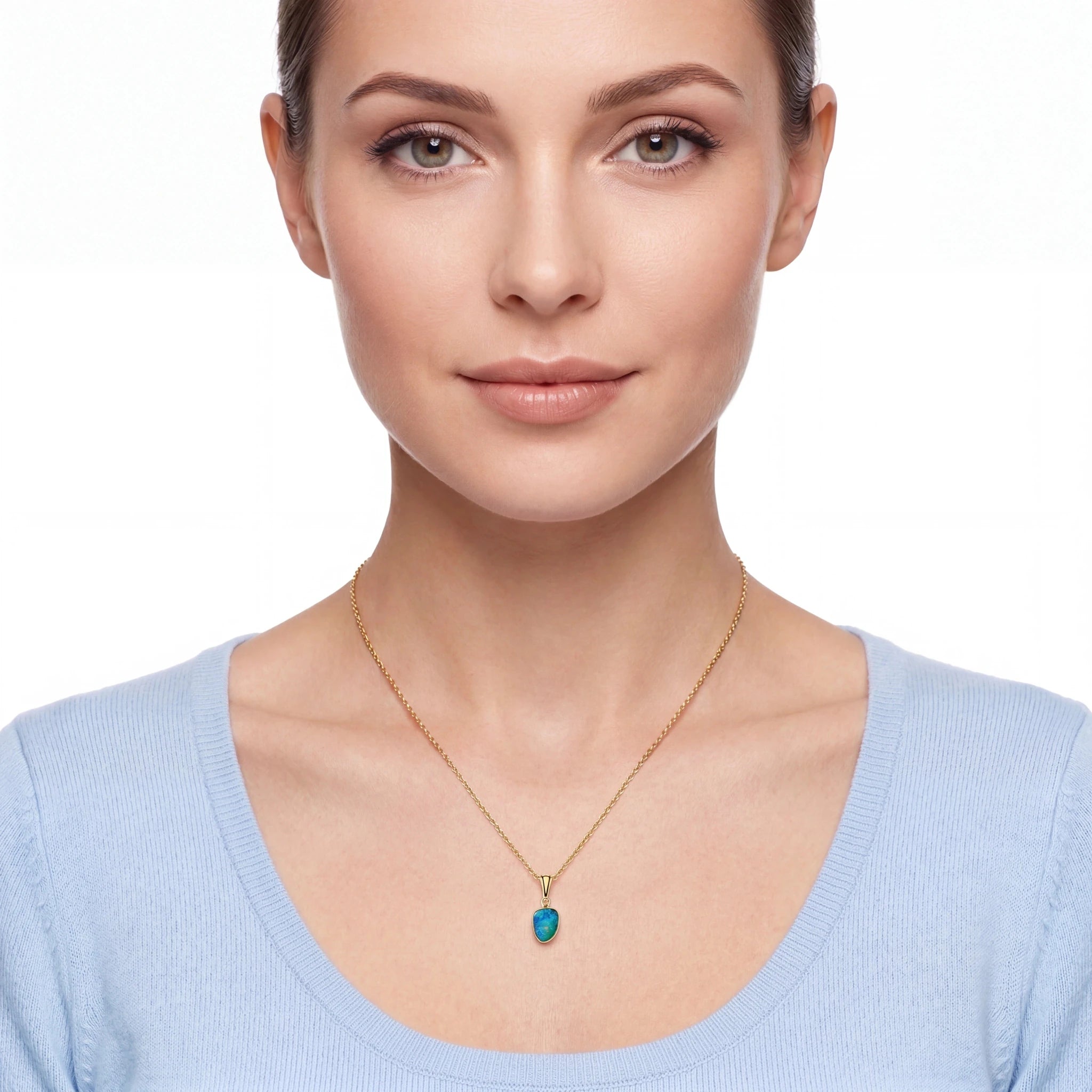 A woman wearing a delicate gold chain necklace with a small, heart-shaped turquoise pendant, shown against a plain white background.
