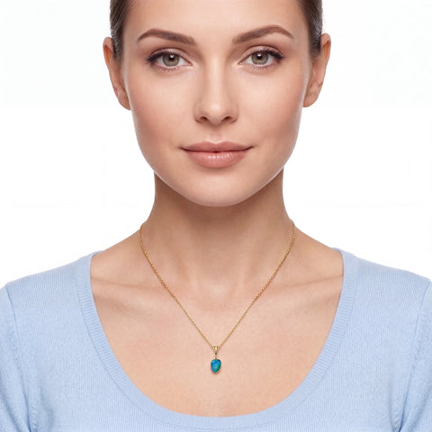 A woman wearing a delicate gold chain necklace with a small, heart-shaped turquoise pendant, shown against a plain white background.