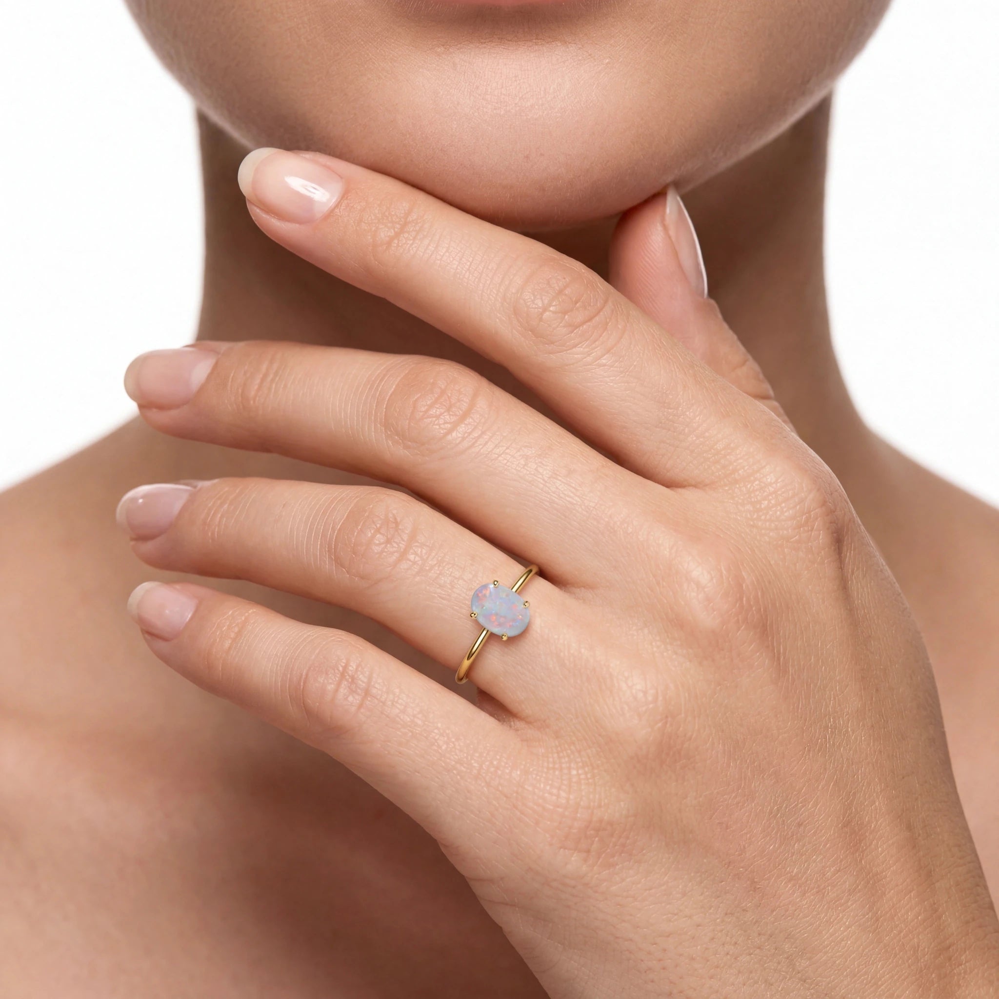 A close-up of a model's hand wearing a delicate gold ring with a small, pale blue-grey opal gemstone.