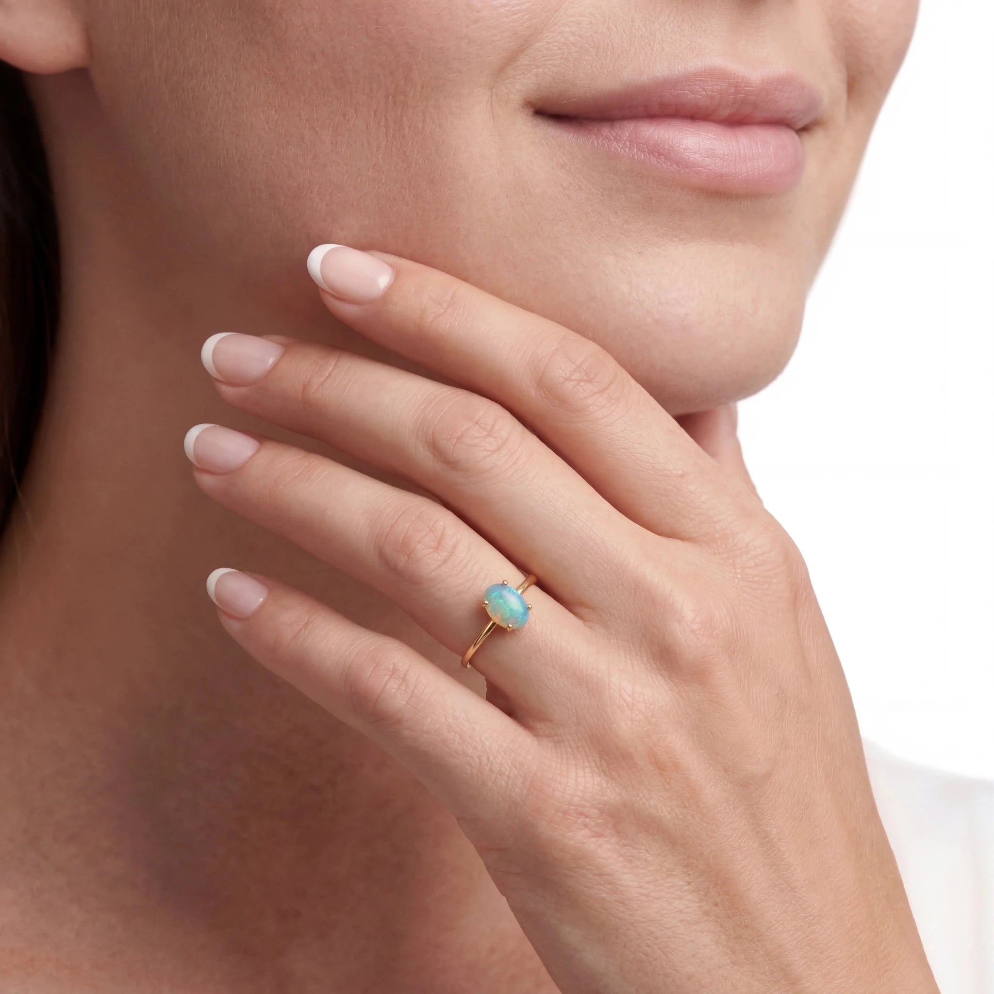 Close-up of a woman wearing a gold ring with an opal stone, touching the chin.
