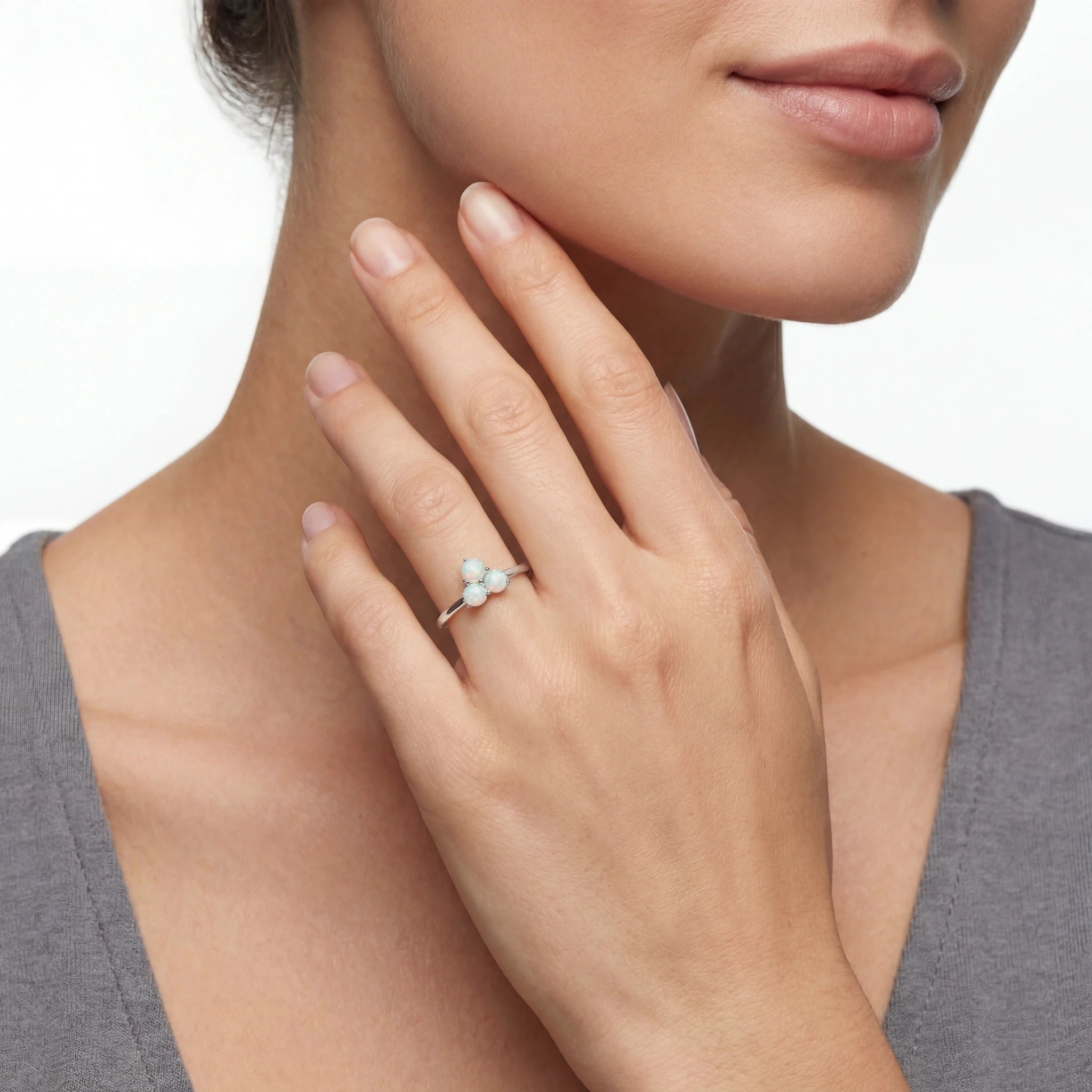 Close-up of a hand wearing a ring with a clear stone, against a neutral background