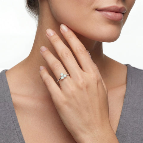 Close-up of a hand wearing a ring with a clear stone, against a neutral background