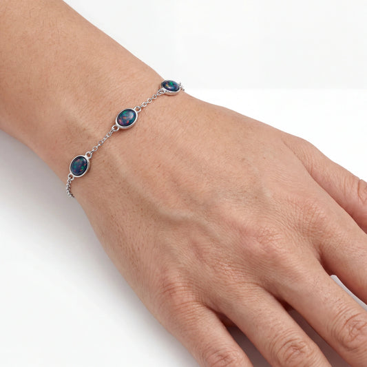 Hand wearing a silver bracelet with multicolour opal gemstones on a white background
