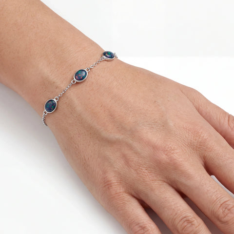 Hand wearing a silver bracelet with multicolour opal gemstones on a white background
