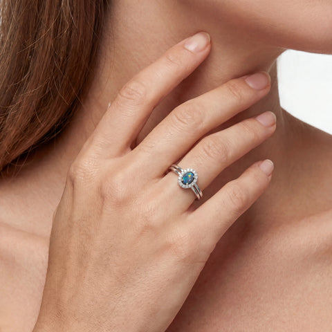 Close-up of a hand wearing a ring with a blue gemstone, touching the neck.