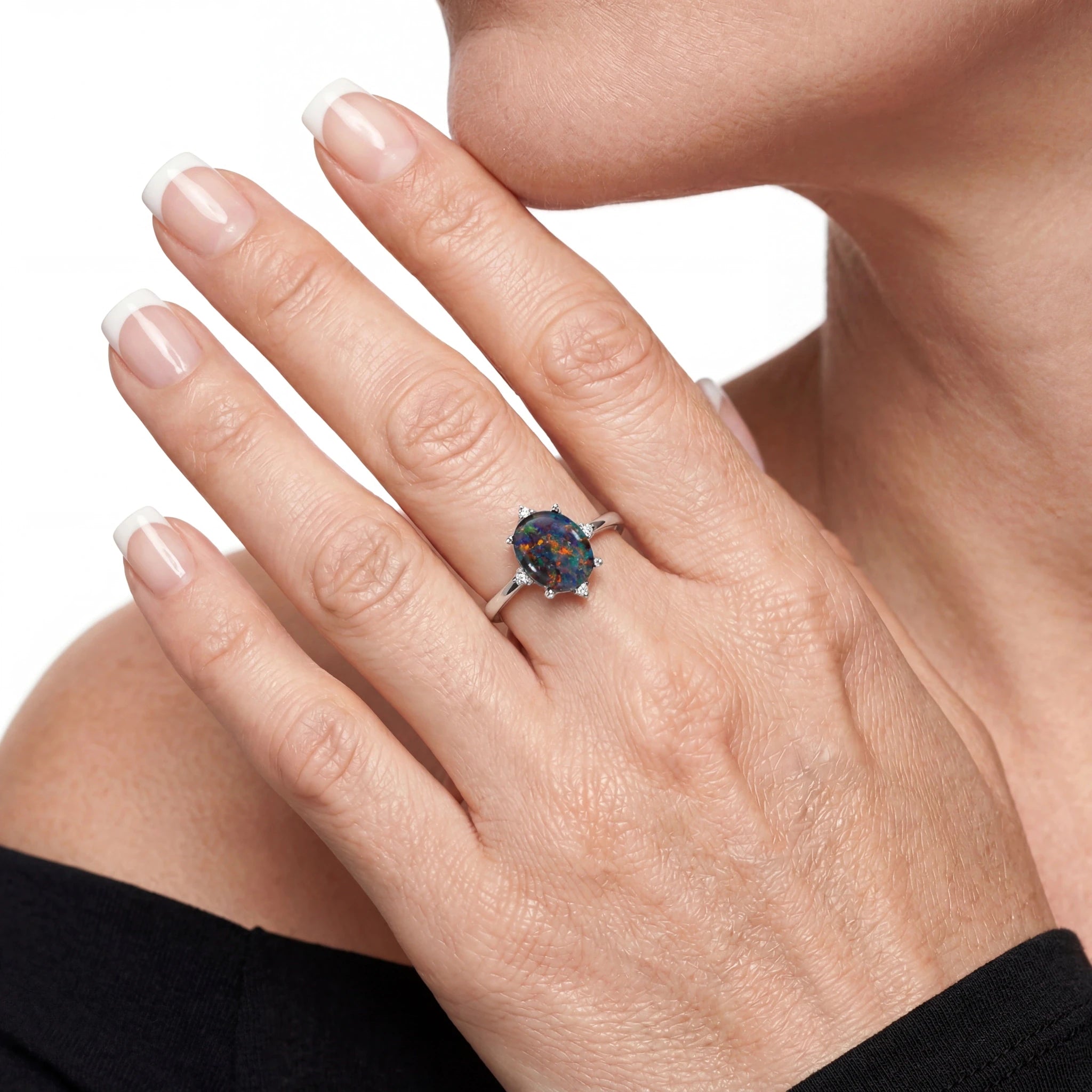 Close-up of a hand wearing a ring with a multicoloured gemstone on a white background