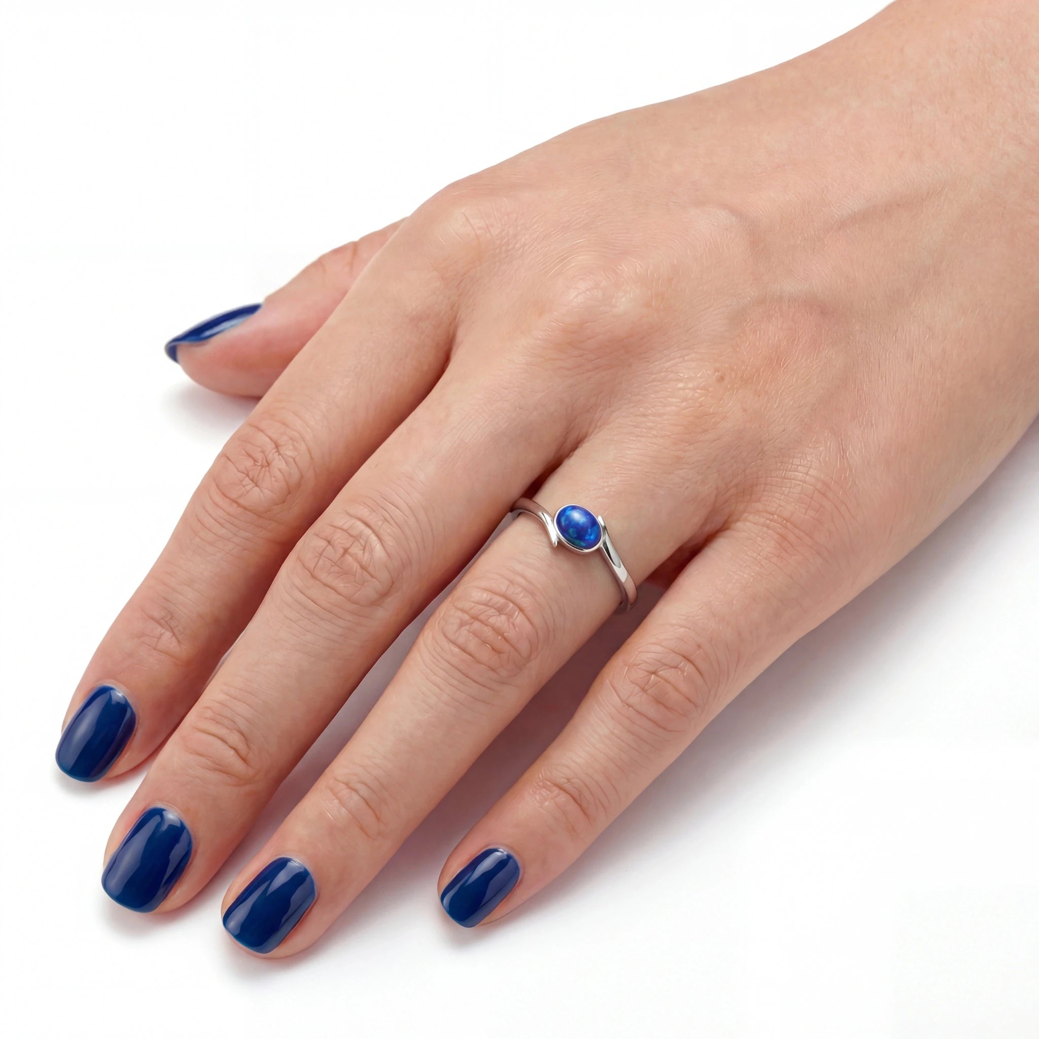 Hand wearing a silver ring with a blue gemstone on a white background