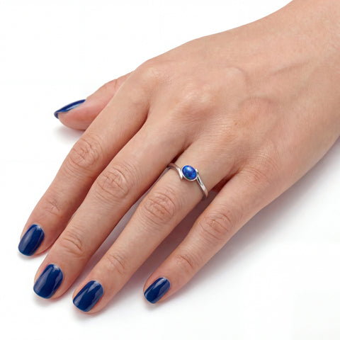 Hand wearing a silver ring with a blue gemstone on a white background