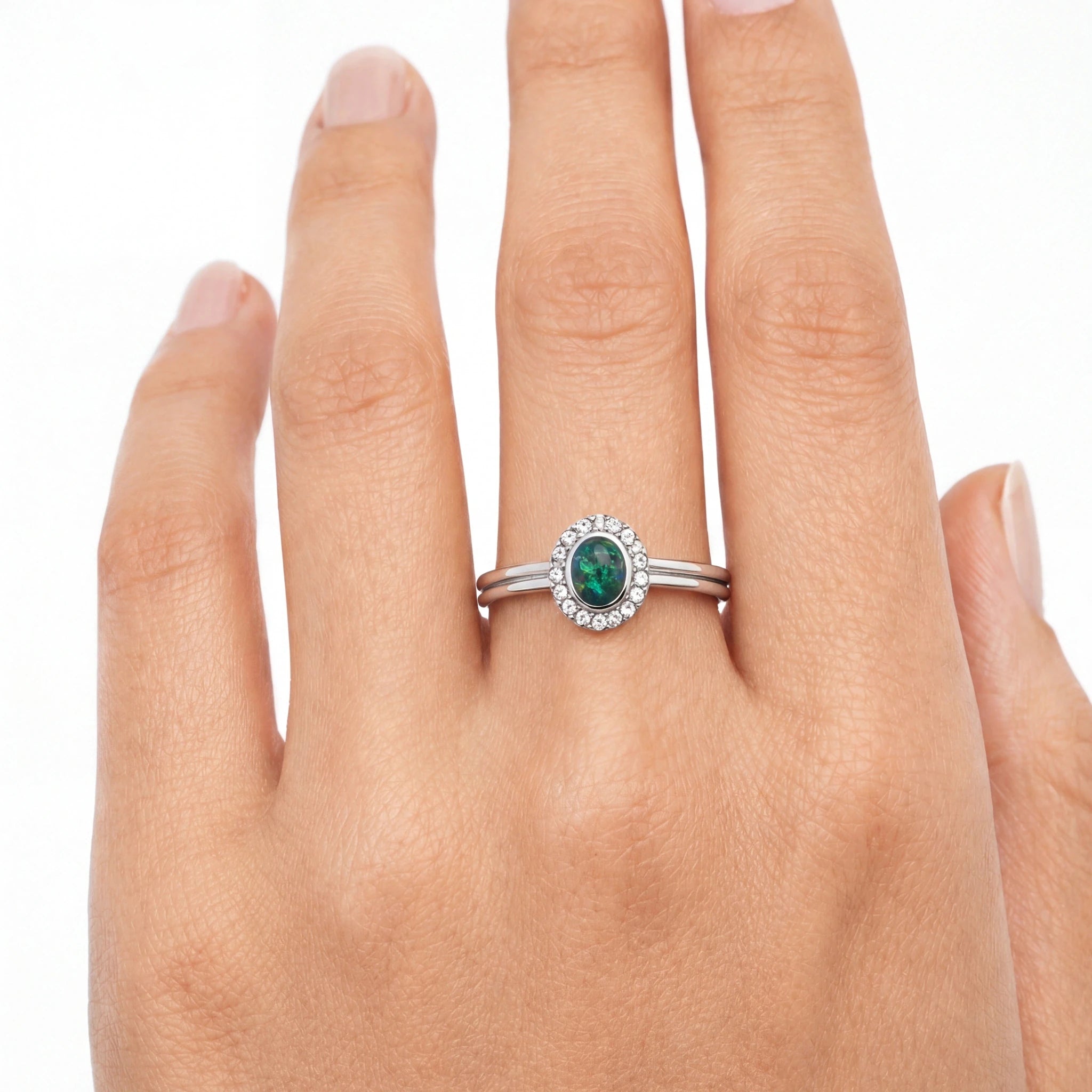 Silver ring with a green gemstone on a hand against a white background