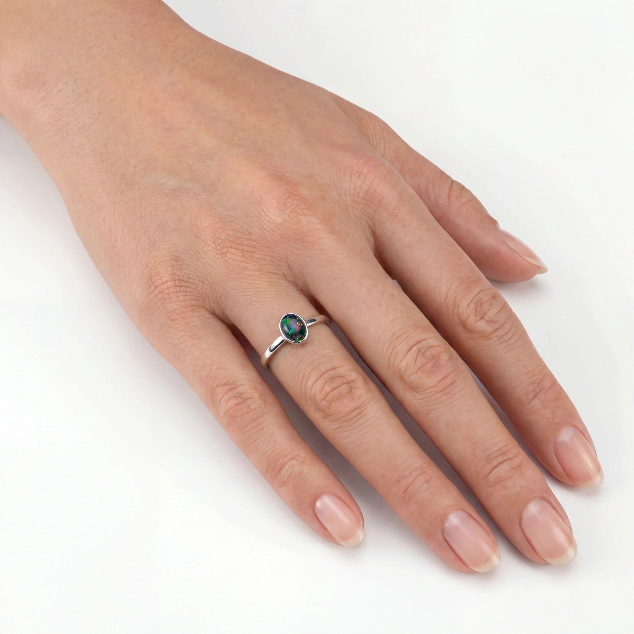 Hand wearing a silver ring with a green gemstone on a white background