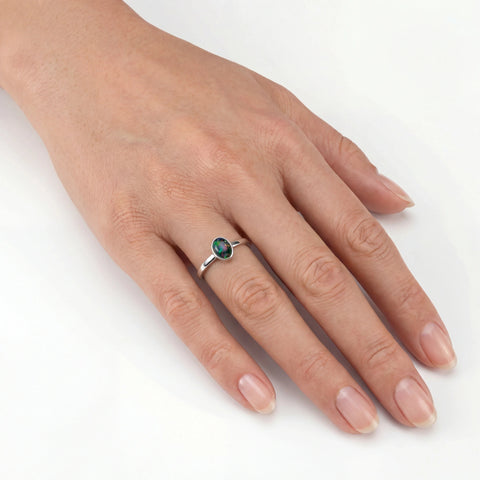 Hand wearing a silver ring with a green gemstone on a white background
