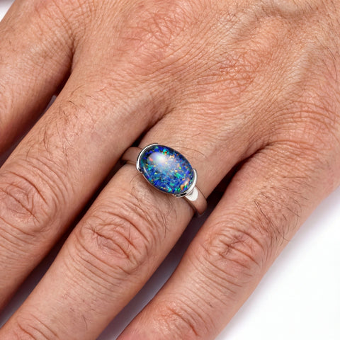 Hand wearing a ring with an opal stone on a neutral background