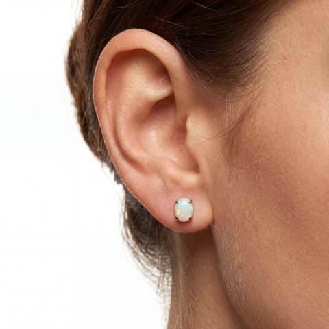 Close-up of an ear wearing a small opal stud earring on a plain background