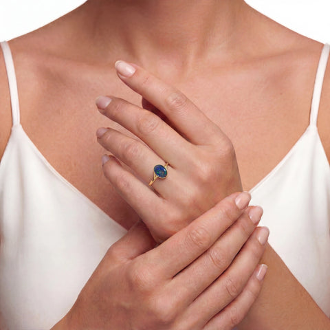 Close-up of a woman's hand wearing a gold ring with a green gemstone, touching her chest.