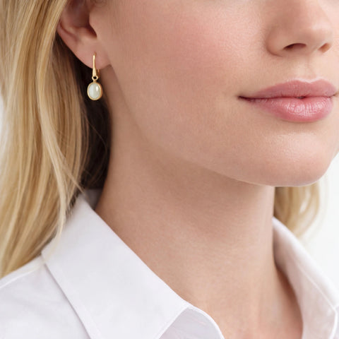 Close-up of a woman wearing gold earrings with a pearl-like stone.