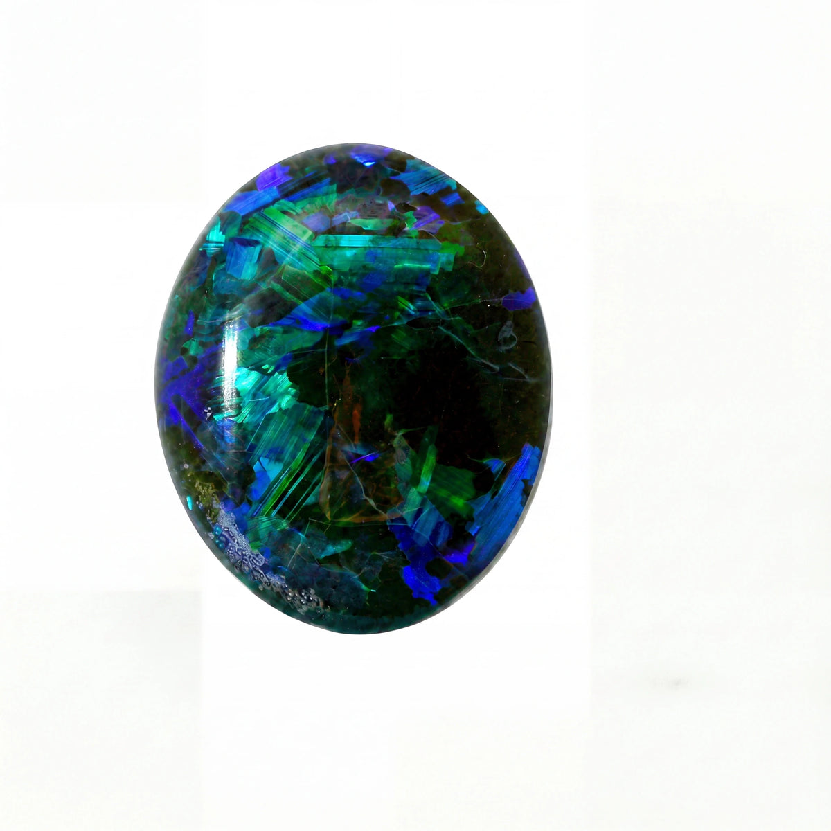 A polished oval cabochon gemstone featuring vibrant iridescent colours including blue, green, and purple over a dark base, set against a plain white background.