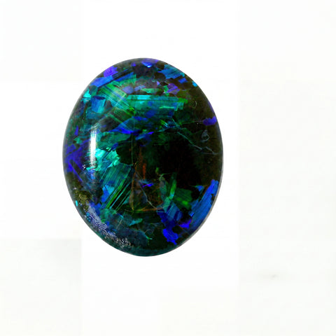 A polished oval cabochon gemstone featuring vibrant iridescent colours including blue, green, and purple over a dark base, set against a plain white background.