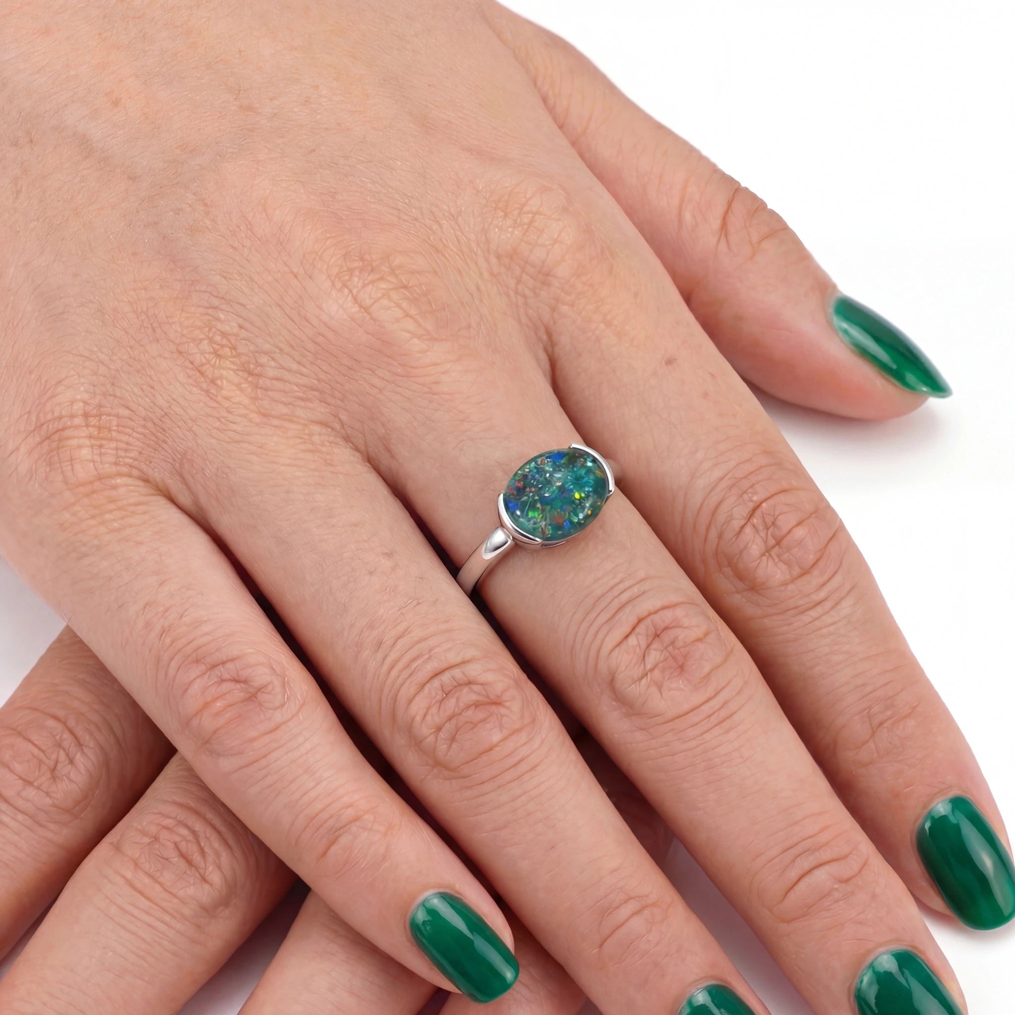 Hand wearing a silver ring with a colourful gemstone on a white background