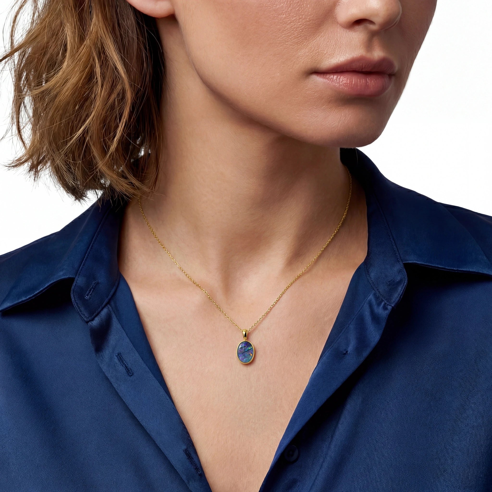 Close-up of a person wearing a gold necklace with a blue pendant against a white background