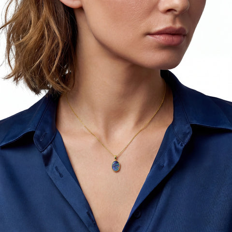 Close-up of a person wearing a gold necklace with a blue pendant against a white background