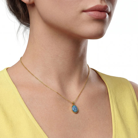 Close-up of a woman wearing a gold necklace with a blue pendant on a white background