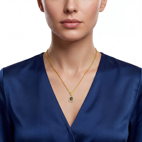 Gold necklace with a pendant on a person wearing a blue top against a white background
