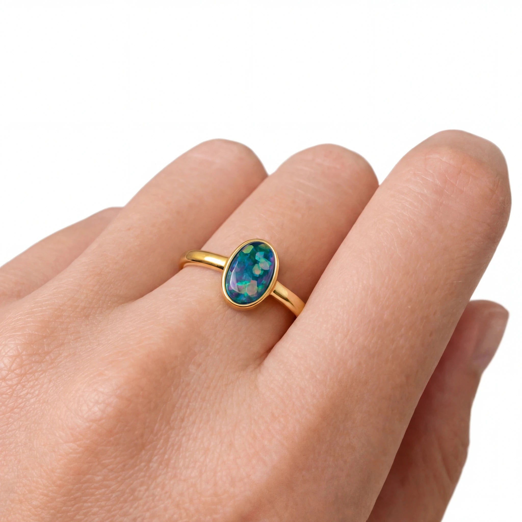 Gold ring with an opal stone on a hand against a white background