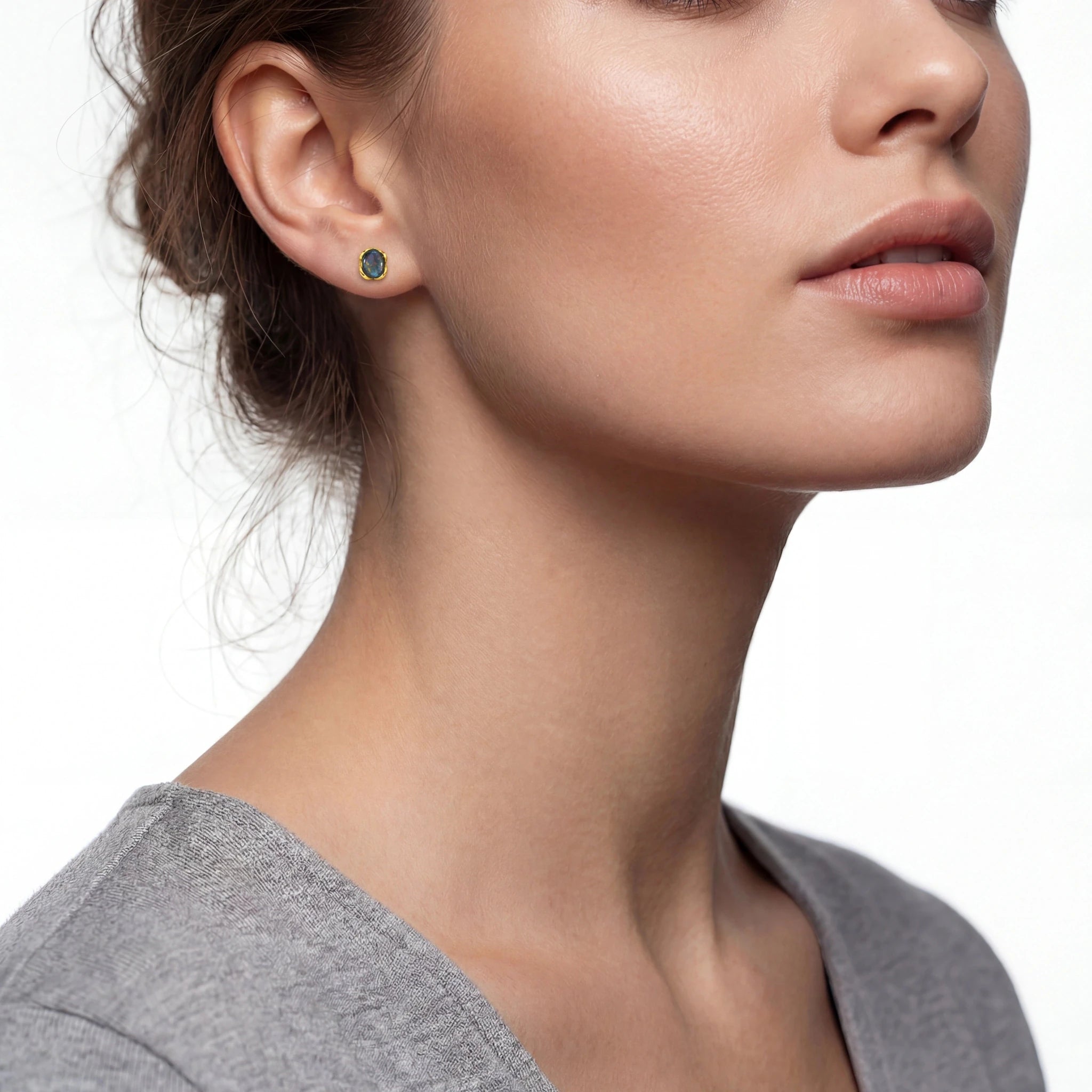 Close-up of a woman wearing a gold earring with a green gemstone on a white background