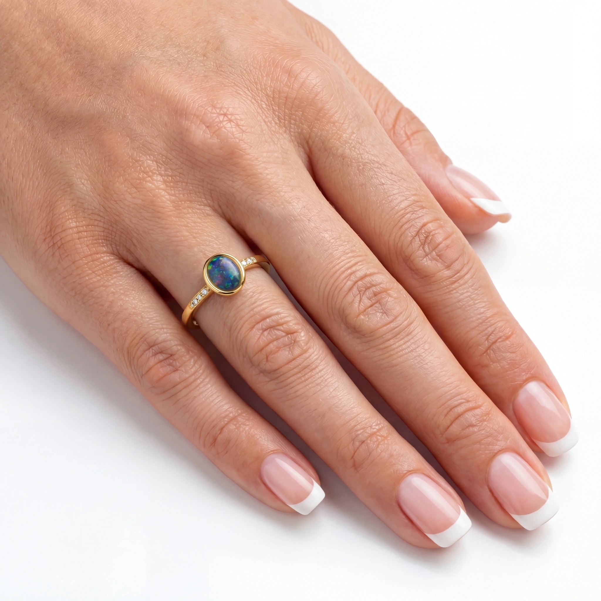 Hand wearing a gold ring with an opal stone on a white background