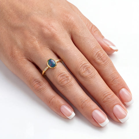 Hand wearing a gold ring with an opal stone on a white background