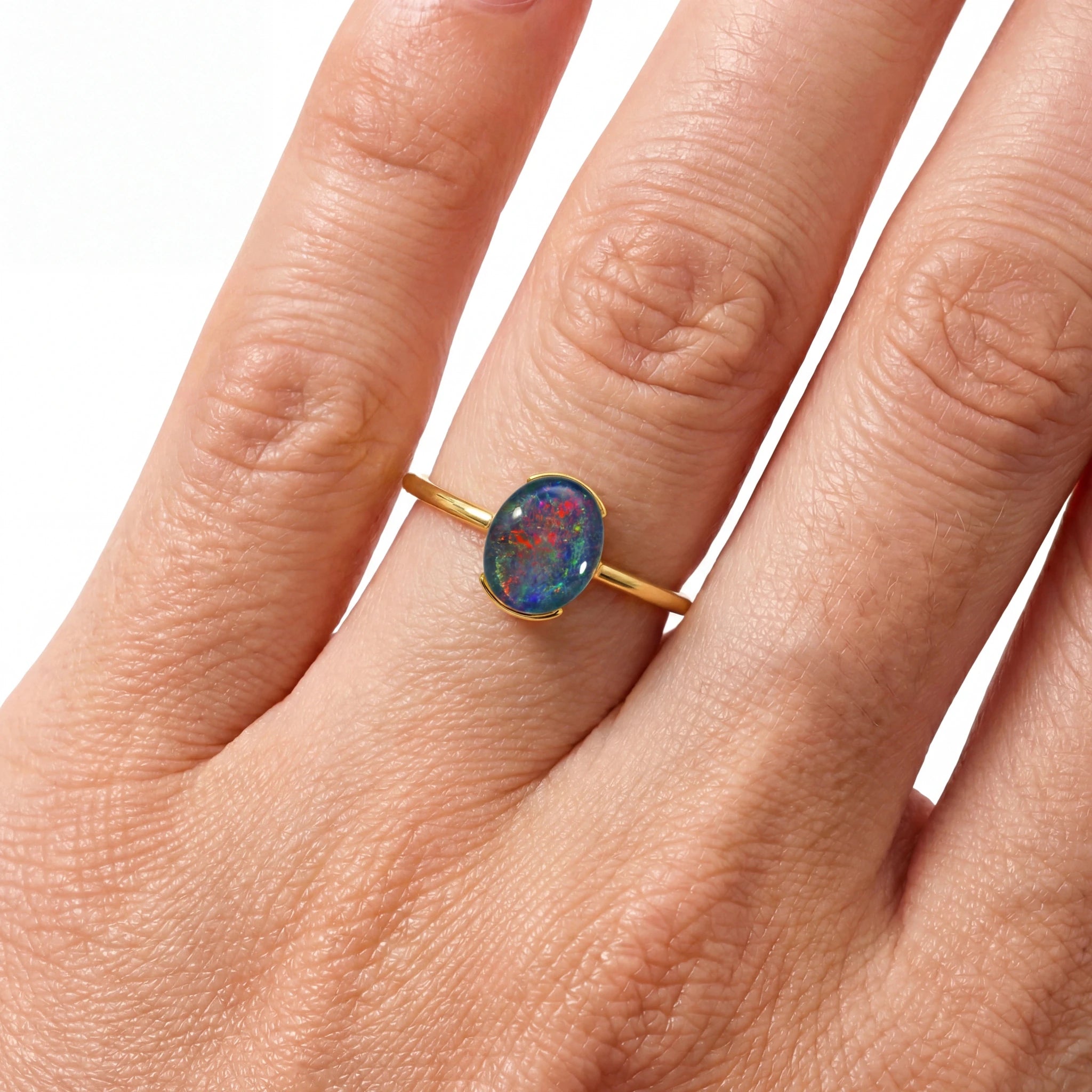 Gold ring with a colourful gemstone on a hand against a white background