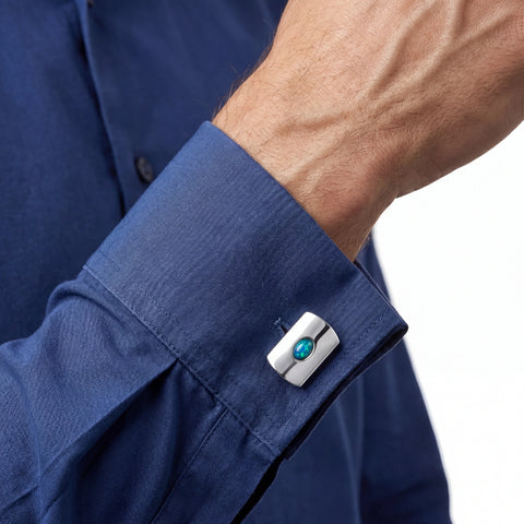 Close-up of a blue shirt cuff with a silver and turquoise cufflink.