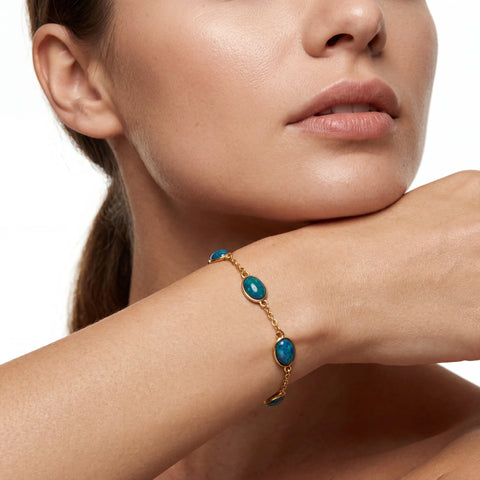 Close-up of a woman's arm wearing a gold bracelet with blue stones on a white background
