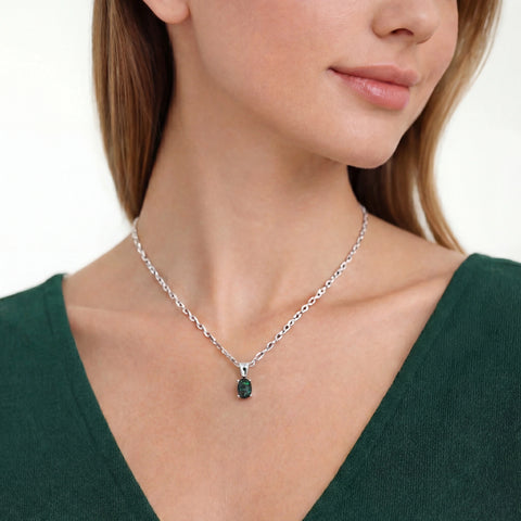 Woman wearing a silver necklace with a green gemstone pendant on a white background