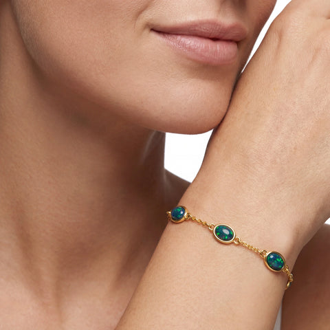 Close-up of a woman's wrist wearing a gold bracelet with green gemstones.