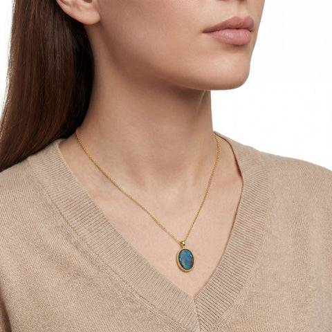 Woman wearing a gold necklace with a blue pendant against a neutral background