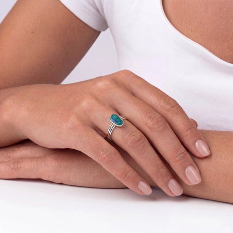 Hand wearing a silver ring with a green gemstone on a white background