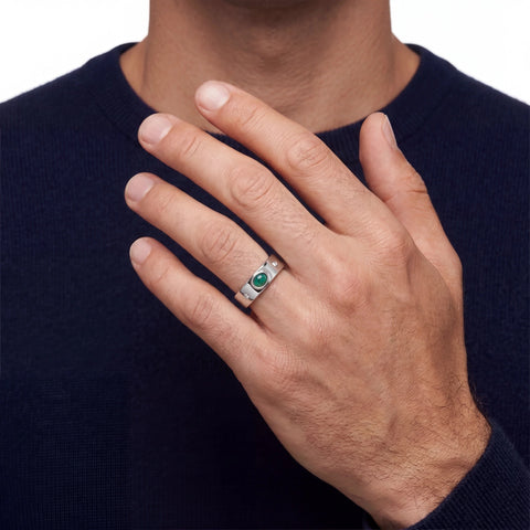 Man wearing a silver ring with a green opal gemstone against a dark blue sweater.