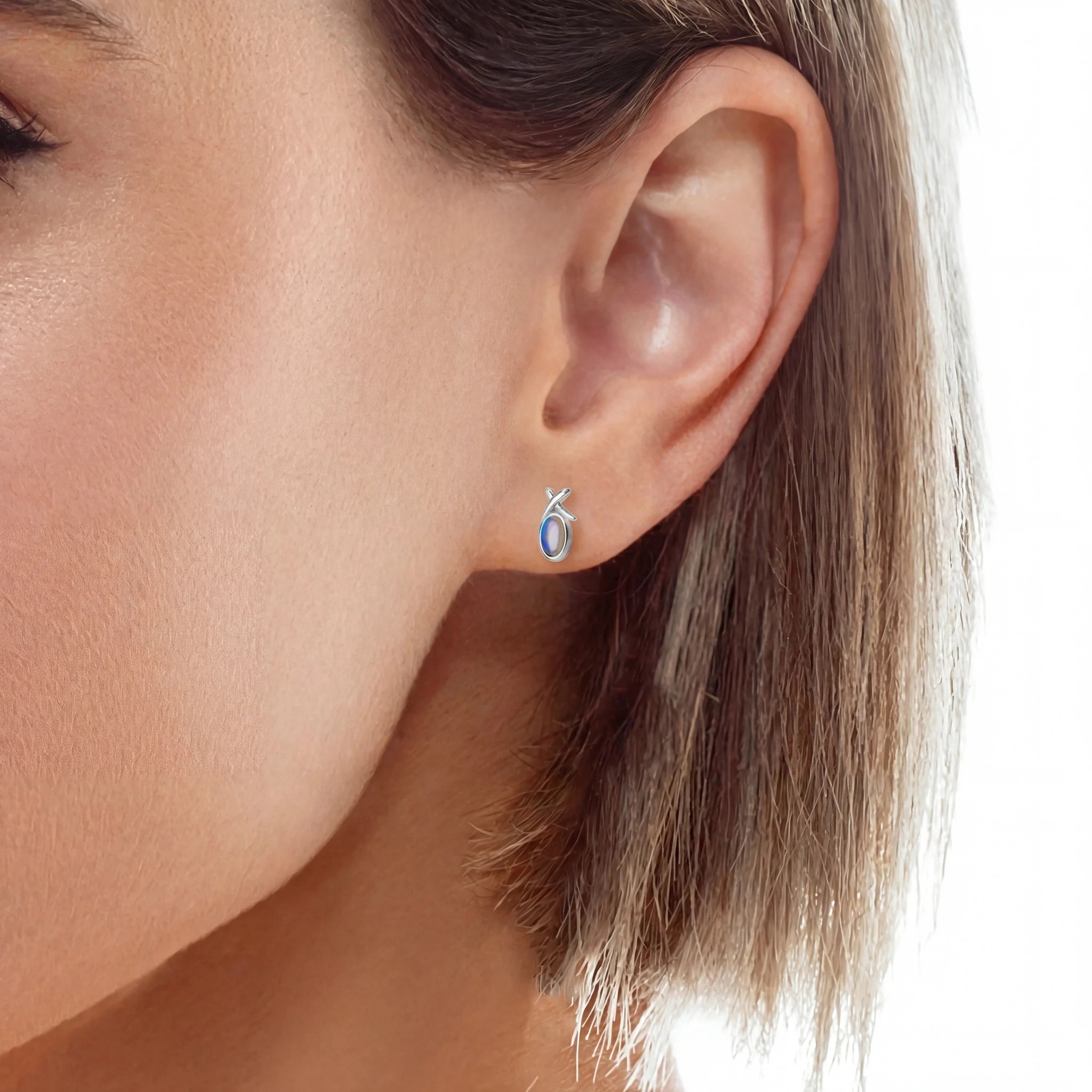 Close-up of an ear wearing a silver earring with a blue gemstone on a white background