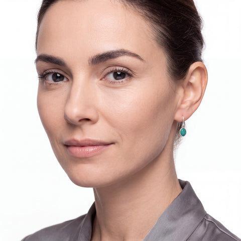Close-up of a woman wearing green earrings with a neutral background