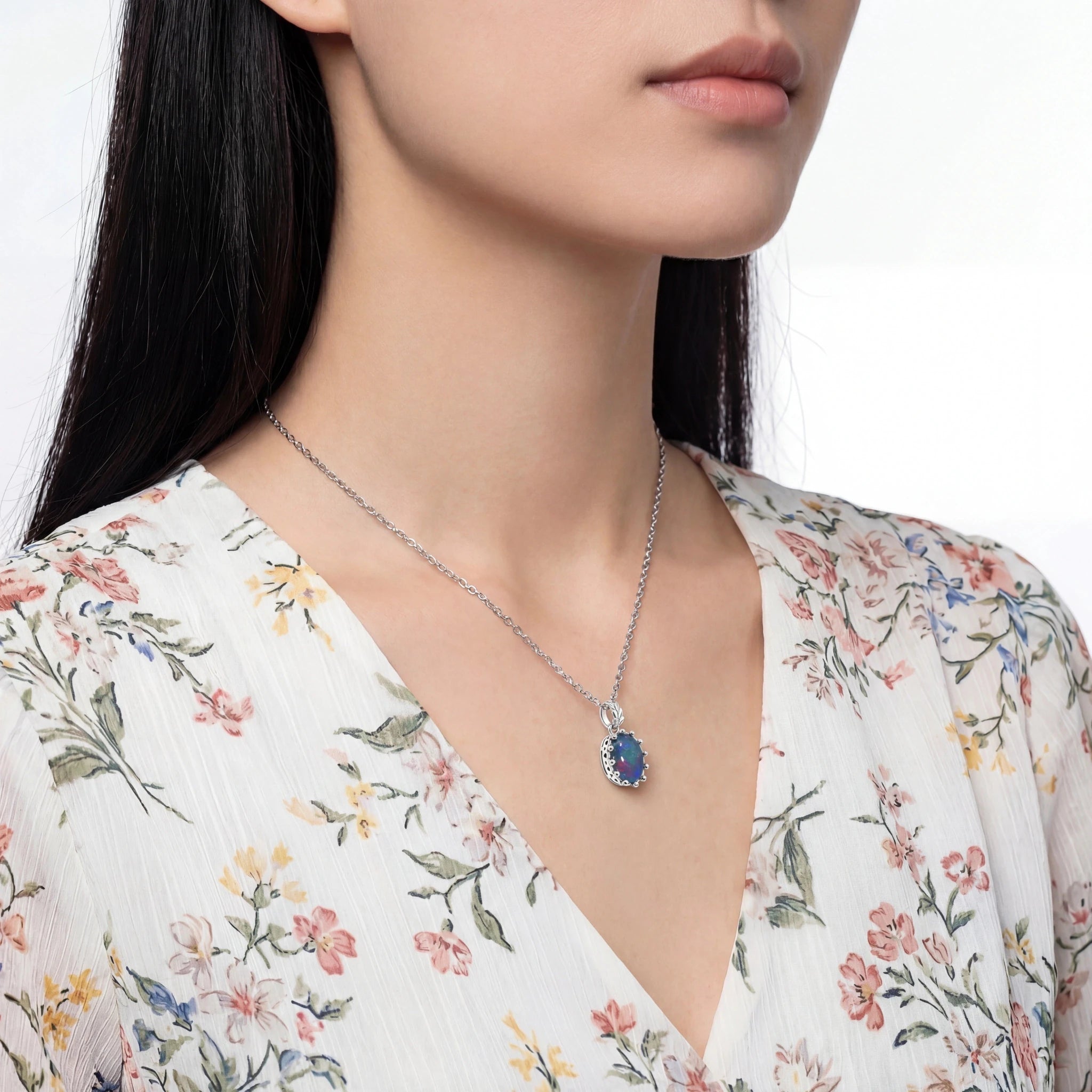 Woman wearing a floral dress with a necklace featuring a blue gemstone pendant.