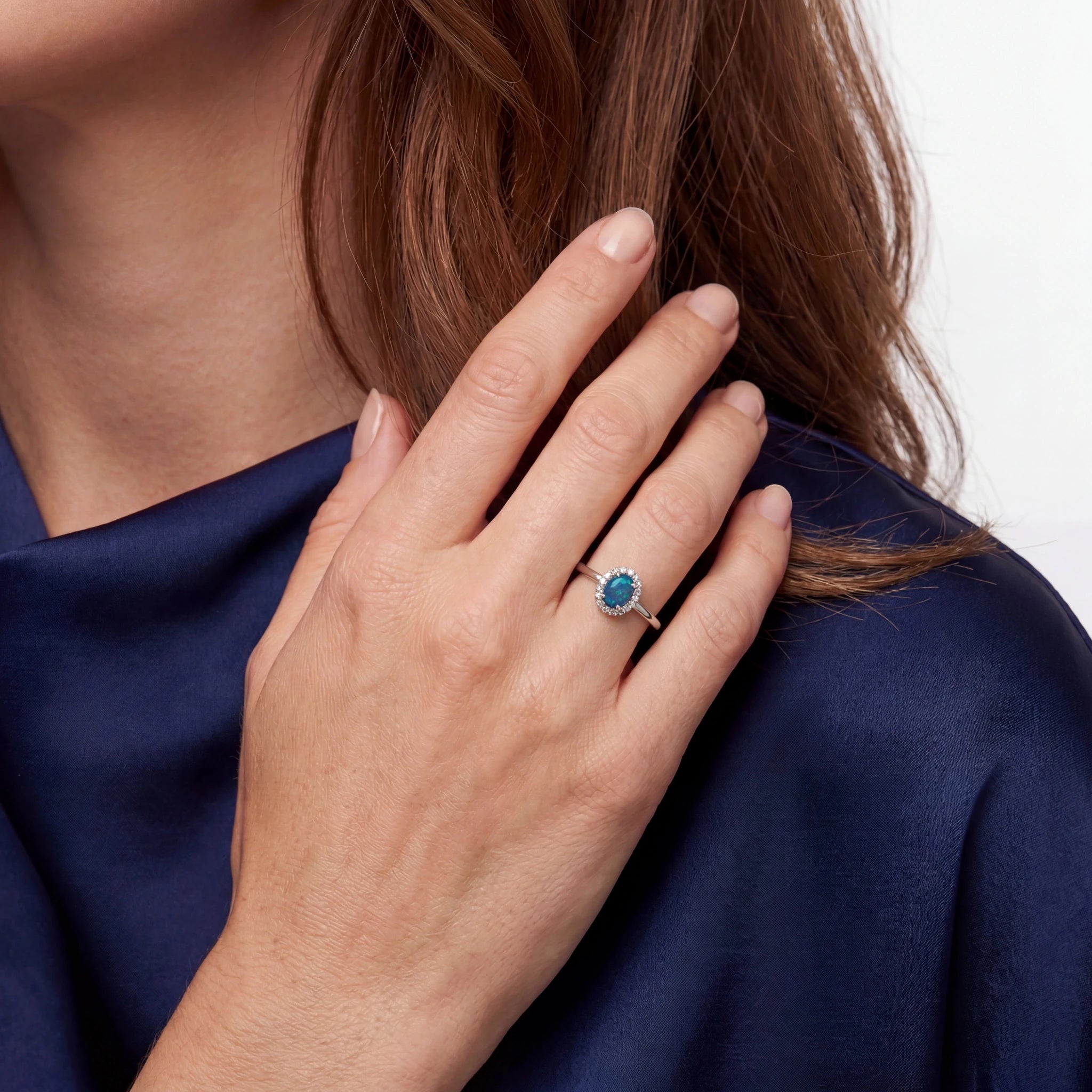 Close-up of a hand wearing a ring with a blue gemstone, against a white background