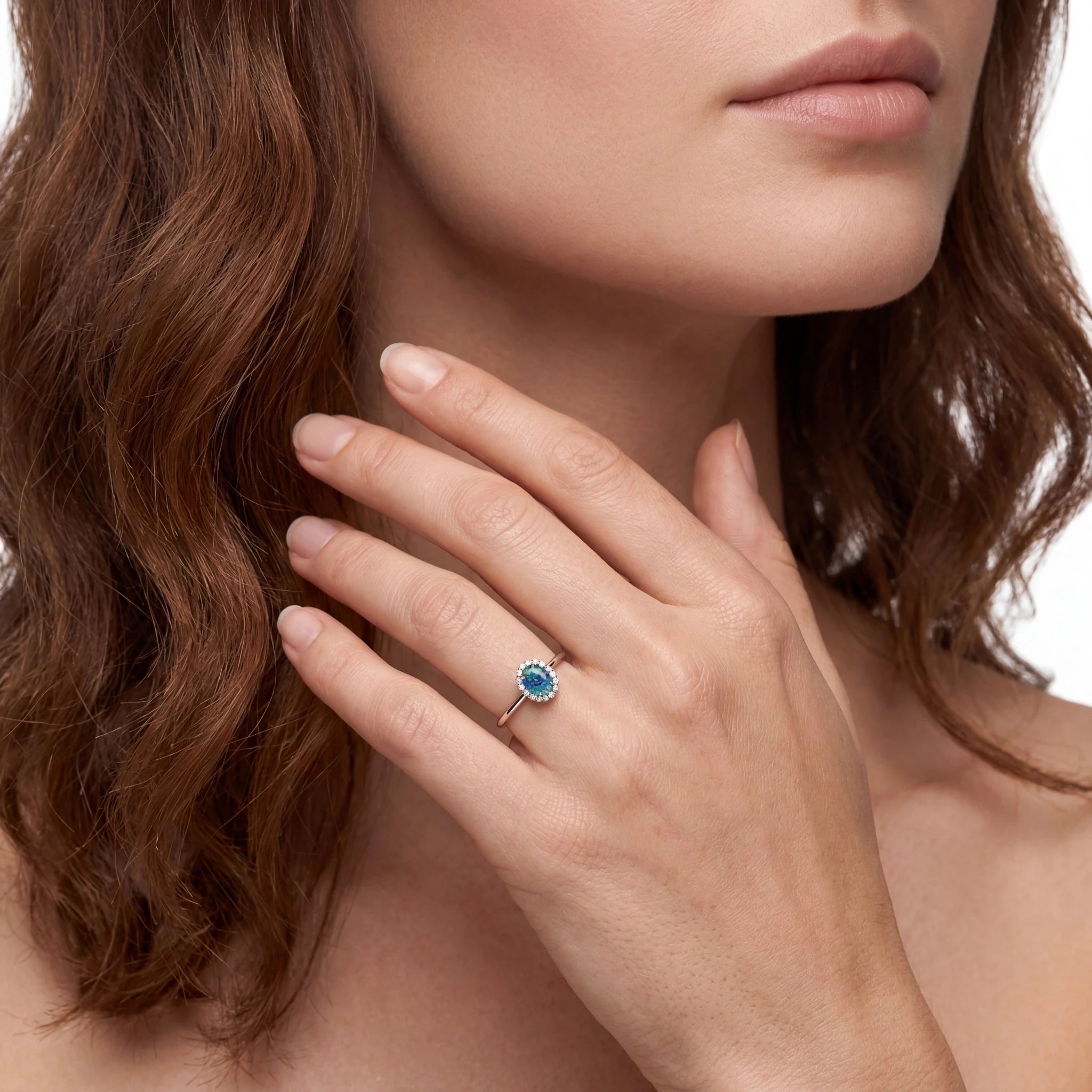 Close-up of a woman's hand wearing a ring with a blue gemstone, touching her neck.
