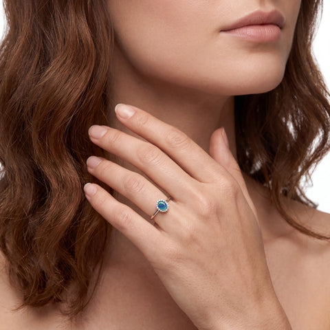 Close-up of a woman's hand wearing a ring with a blue gemstone, touching her neck.