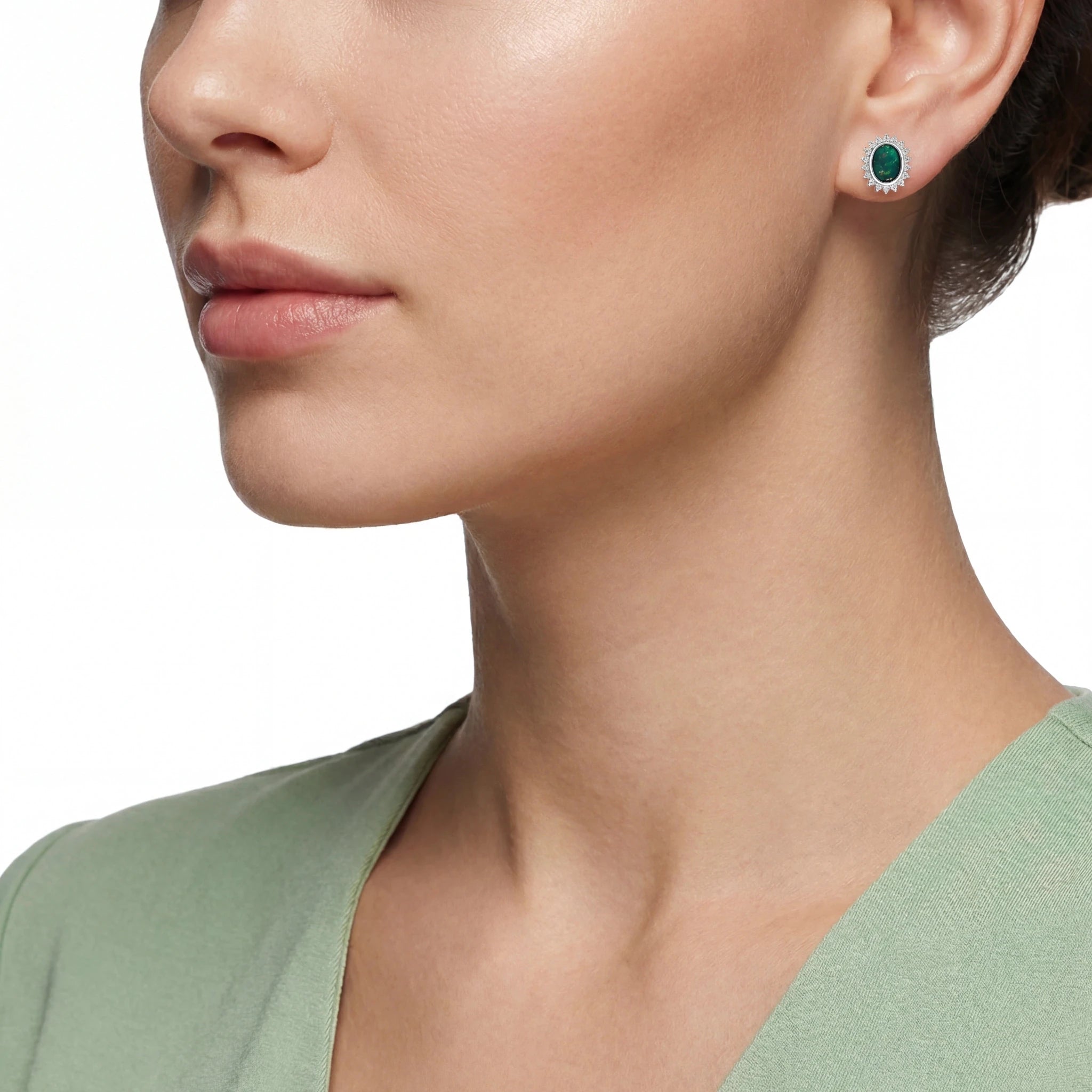 Close-up of a woman wearing green gemstone earrings with a plain background