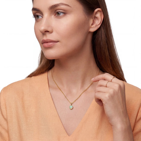 Woman wearing a gold necklace with a small pendant on a plain background