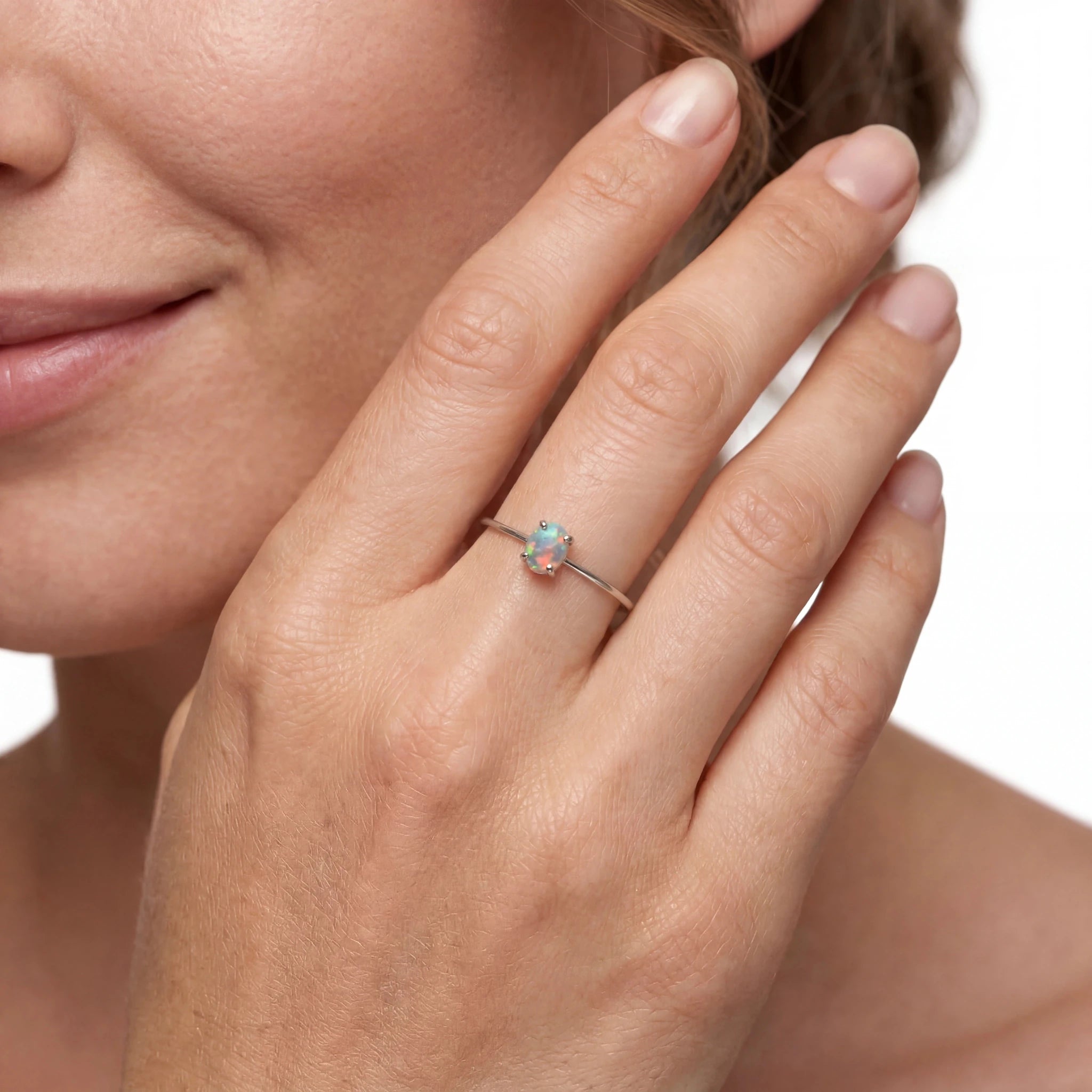 Close-up of a hand wearing a ring with a colourful gemstone on a neutral background