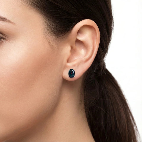 Close-up of a woman's ear wearing a blue gemstone earring on a white background