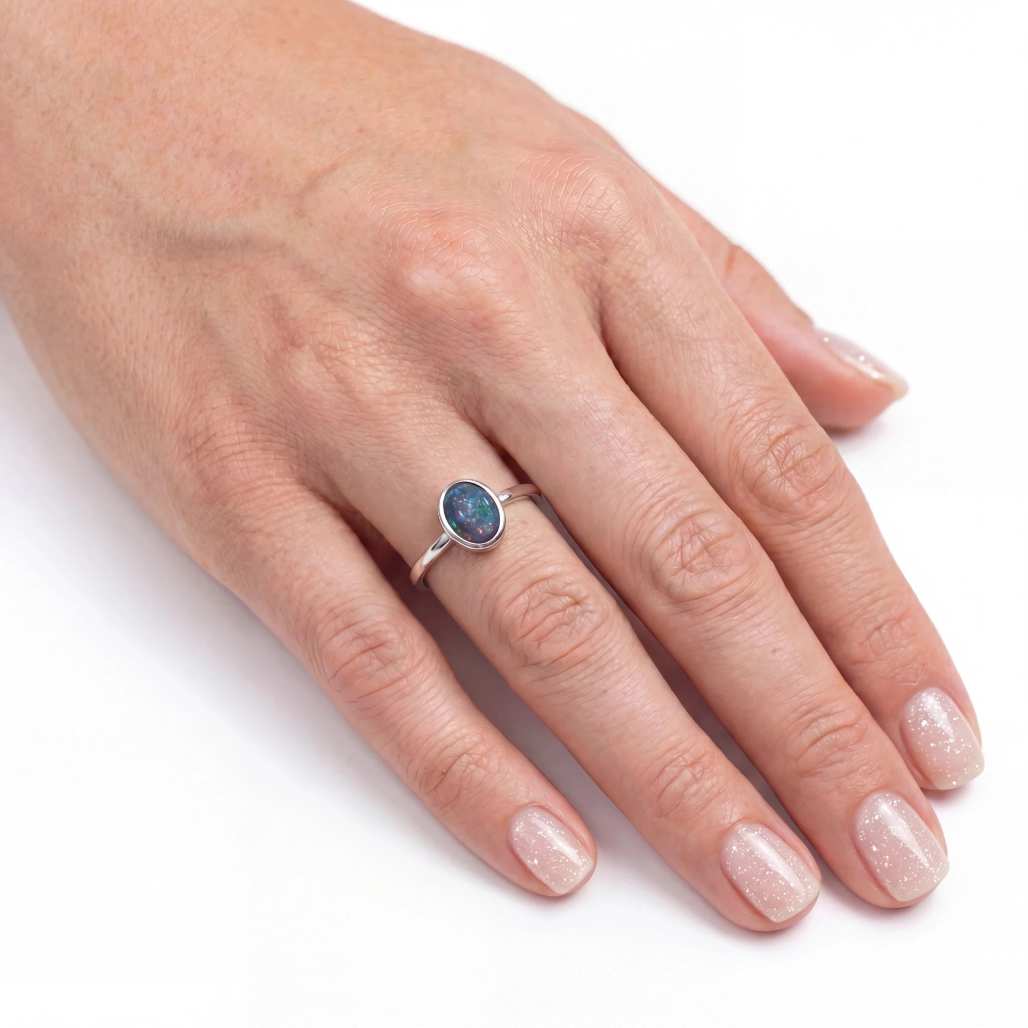 Hand wearing a ring with an opal stone on a white background